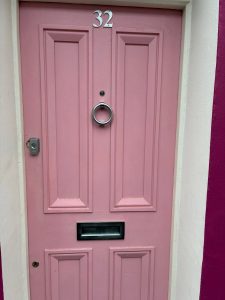 A pink door with furnishings: a house number, door knocker, letterbox, escutcheon