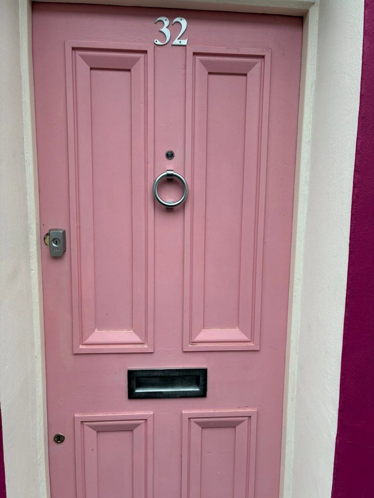 A pink door with furnishings: a house number, door knocker, letterbox, escutcheon