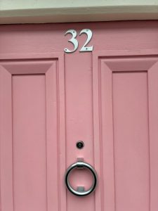 Door knocker and House number in brushed satin finish against a pink door
