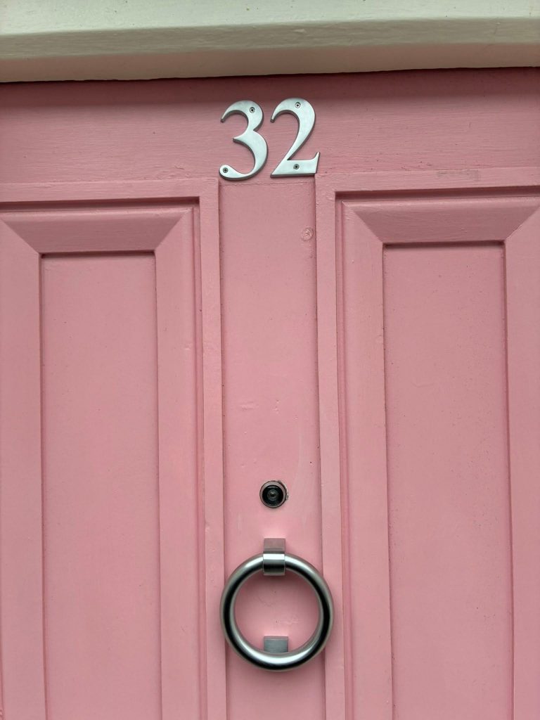 Door knocker and House number in brushed satin finish against a pink door